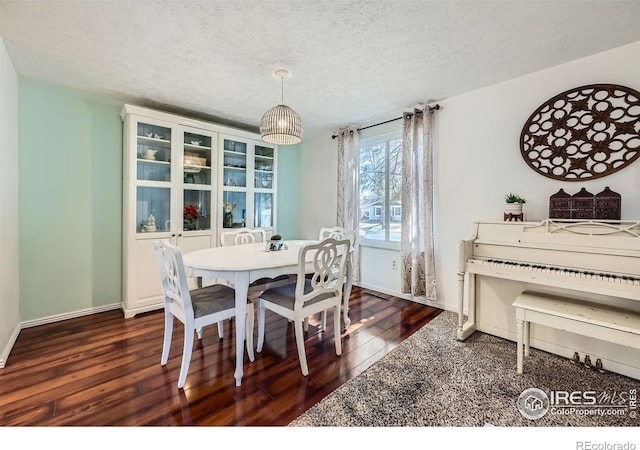 dining area with a textured ceiling, baseboards, and dark wood-type flooring