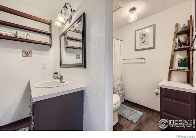 bathroom with toilet, vanity, a textured ceiling, wood finished floors, and baseboards