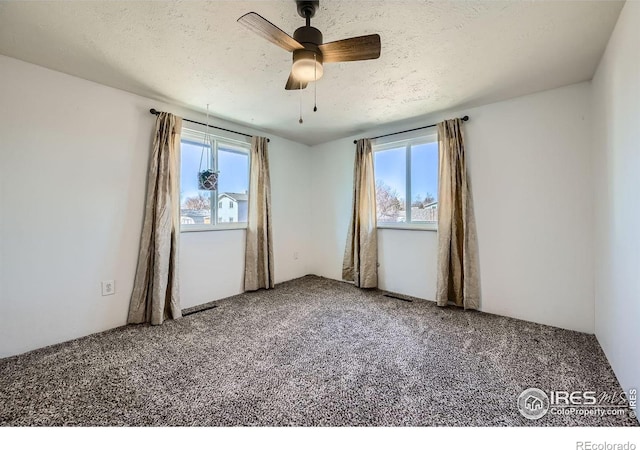 empty room featuring plenty of natural light, carpet, ceiling fan, and a textured ceiling