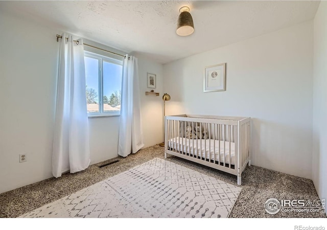 carpeted bedroom featuring a nursery area and visible vents