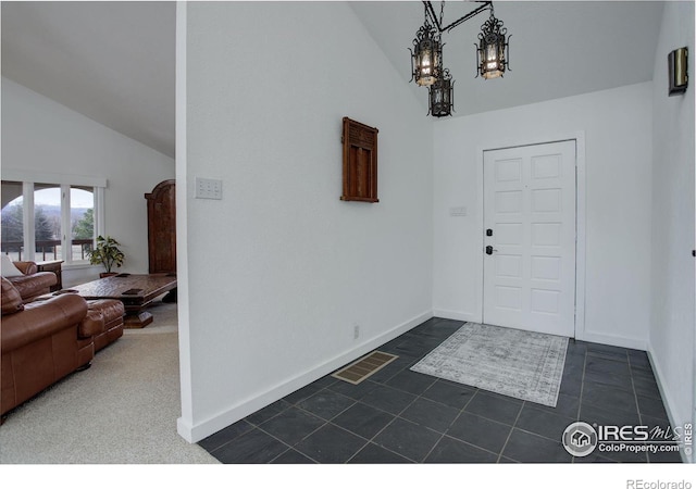 foyer entrance with high vaulted ceiling, dark tile patterned floors, visible vents, baseboards, and an inviting chandelier