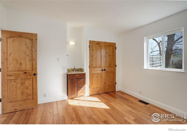 unfurnished bedroom featuring baseboards, a sink, visible vents, and light wood-style floors