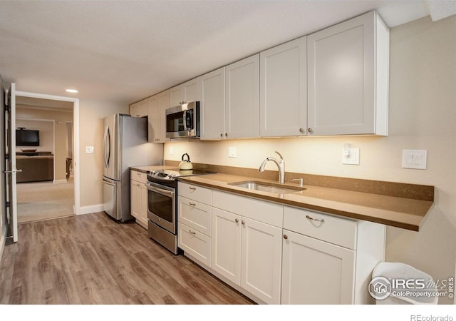 kitchen with stainless steel appliances, light wood-style floors, white cabinets, a sink, and baseboards