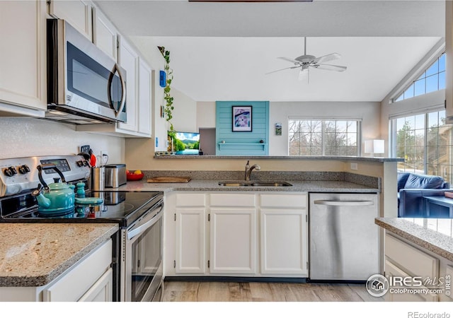 kitchen with light wood-style flooring, appliances with stainless steel finishes, white cabinets, vaulted ceiling, and a sink