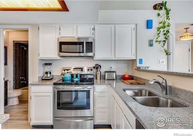 kitchen featuring light wood finished floors, appliances with stainless steel finishes, light stone counters, white cabinetry, and a sink