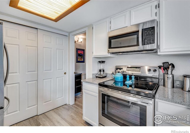 kitchen with stainless steel appliances, light stone counters, light wood-type flooring, and white cabinets