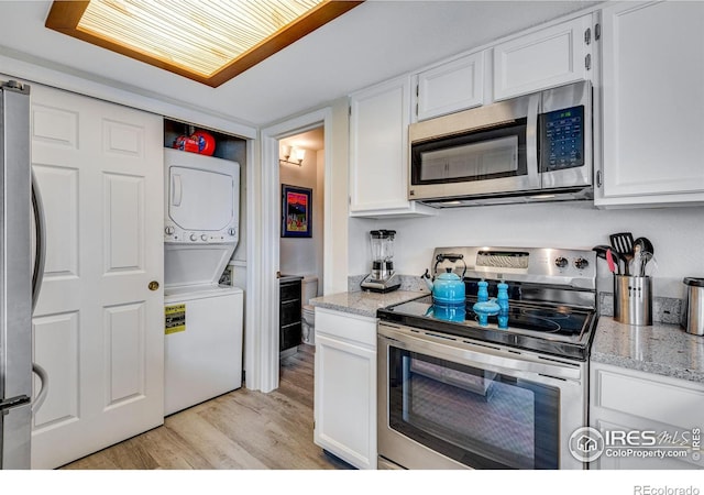 kitchen featuring stacked washer / dryer, white cabinets, appliances with stainless steel finishes, light wood-type flooring, and light stone countertops