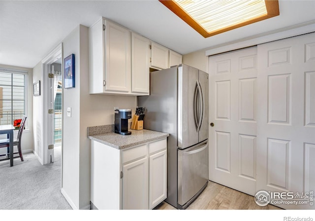 kitchen with light wood finished floors, baseboards, white cabinets, light colored carpet, and freestanding refrigerator