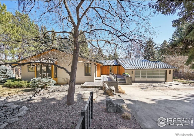 view of front of home with stucco siding, concrete driveway, an attached garage, a standing seam roof, and metal roof