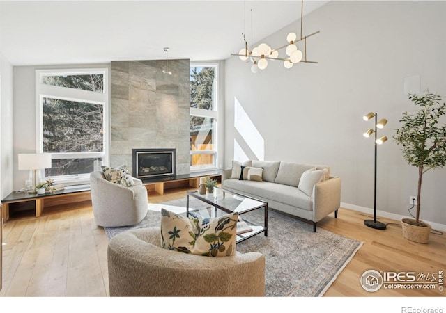 living area featuring high vaulted ceiling, a tile fireplace, baseboards, and wood finished floors