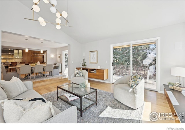 living area with lofted ceiling, light wood-style floors, baseboards, and a chandelier