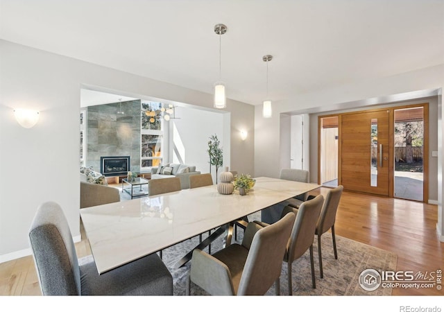 dining space featuring baseboards, a tiled fireplace, and light wood finished floors