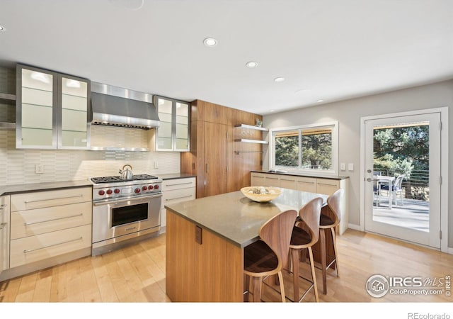 kitchen with light wood-style flooring, premium stove, wall chimney exhaust hood, and open shelves