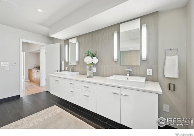 full bath featuring double vanity, tasteful backsplash, a sink, wood finished floors, and baseboards