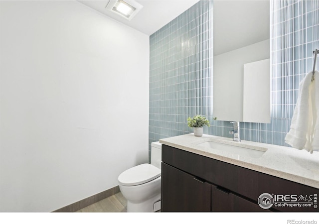 half bath with toilet, vanity, baseboards, visible vents, and tile walls