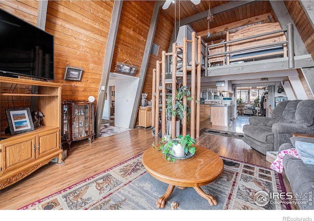 living area featuring beam ceiling, wood walls, wood finished floors, high vaulted ceiling, and wooden ceiling