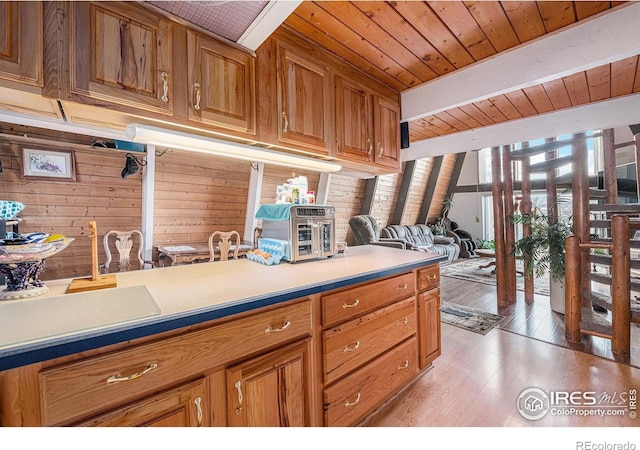 kitchen with wooden ceiling, light wood-style flooring, wooden walls, brown cabinets, and beamed ceiling