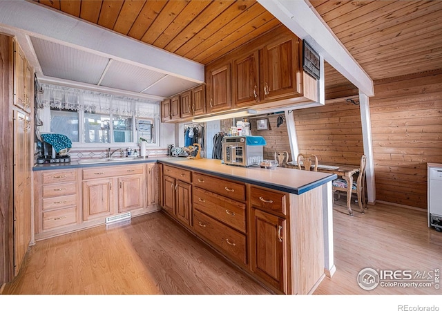 kitchen with wooden walls, beamed ceiling, and light wood-style flooring