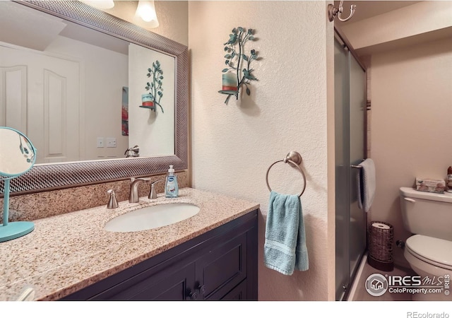 bathroom featuring toilet, a textured wall, vanity, and a stall shower