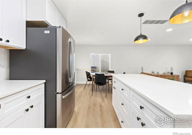 kitchen featuring light wood finished floors, light countertops, visible vents, freestanding refrigerator, and white cabinetry