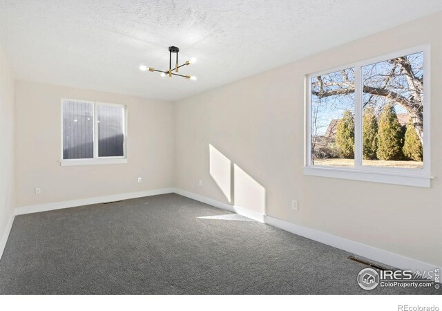 carpeted spare room featuring a notable chandelier, baseboards, and a textured ceiling