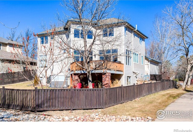 back of house featuring a fenced front yard, brick siding, and a balcony