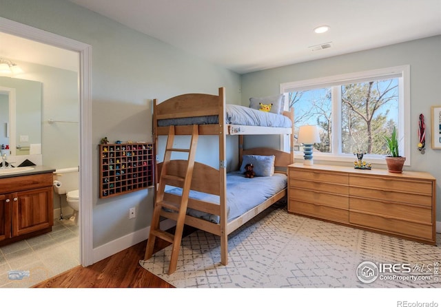 bedroom featuring visible vents, light wood-style floors, connected bathroom, a sink, and baseboards