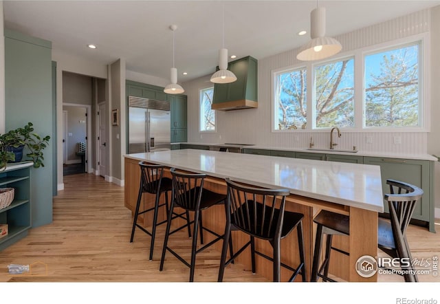 kitchen featuring built in fridge, a sink, green cabinets, light wood-type flooring, and custom exhaust hood