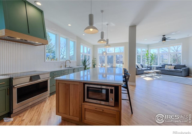 kitchen featuring light wood finished floors, custom range hood, appliances with stainless steel finishes, a sink, and green cabinetry