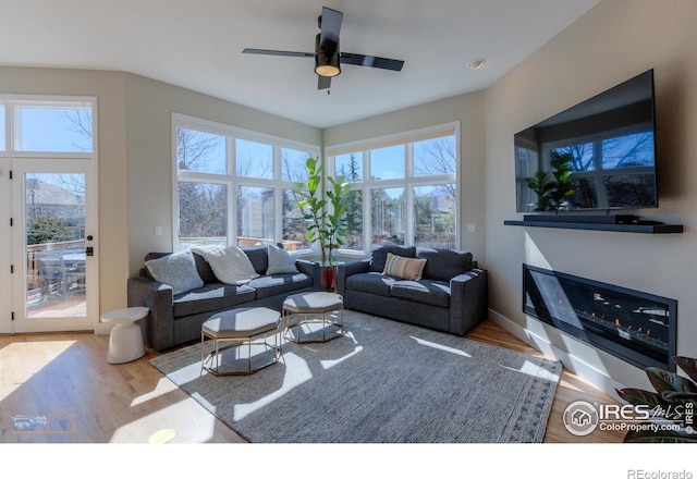 living room featuring ceiling fan, a glass covered fireplace, wood finished floors, and baseboards