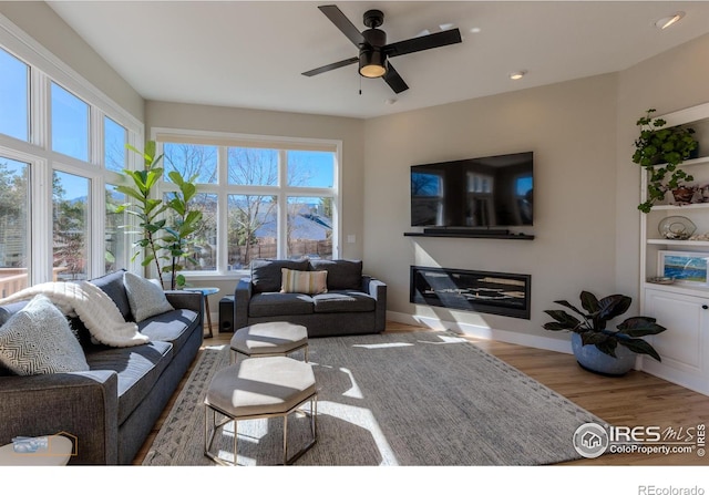 living room with ceiling fan, baseboards, wood finished floors, and a glass covered fireplace