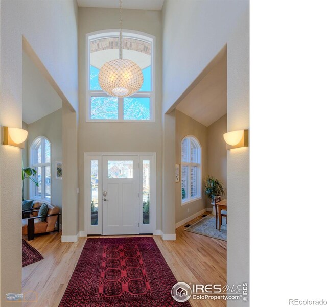 foyer entrance with a chandelier, a towering ceiling, baseboards, and wood finished floors