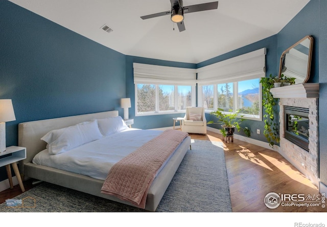 bedroom featuring ceiling fan, wood finished floors, visible vents, baseboards, and a glass covered fireplace