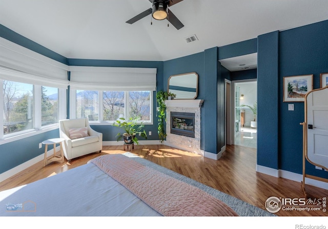 bedroom with a stone fireplace, wood finished floors, visible vents, and baseboards