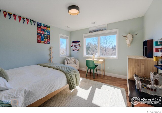 bedroom with baseboards, visible vents, and wood finished floors