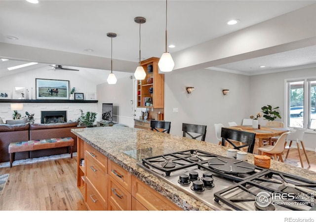 kitchen featuring pendant lighting, a fireplace, stainless steel gas cooktop, light wood-style flooring, and ceiling fan