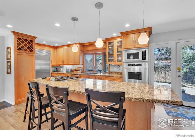 kitchen with recessed lighting, light wood-style flooring, glass insert cabinets, a sink, and built in appliances