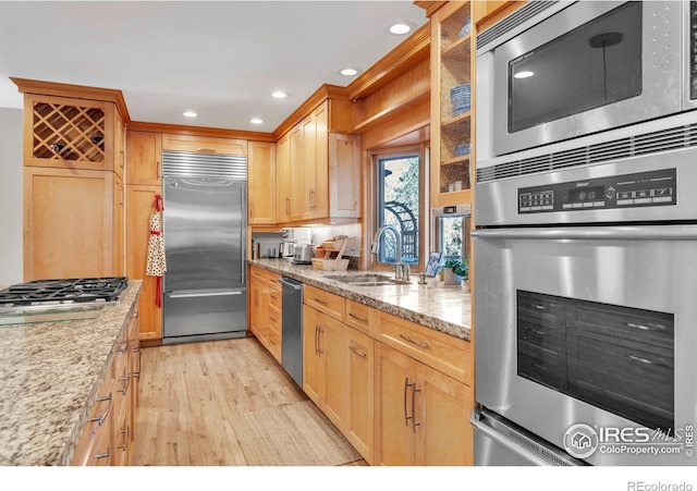 kitchen with built in appliances, light stone counters, a sink, light wood-style floors, and glass insert cabinets