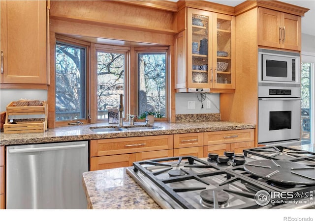 kitchen with stainless steel appliances, a sink, glass insert cabinets, and light stone countertops