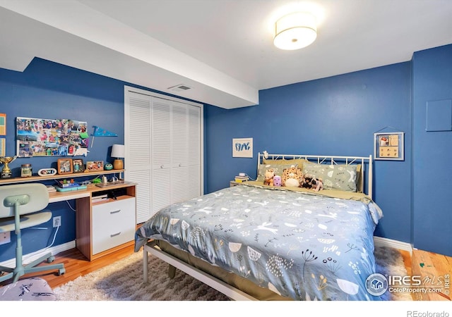 bedroom with baseboards, visible vents, a closet, and wood finished floors