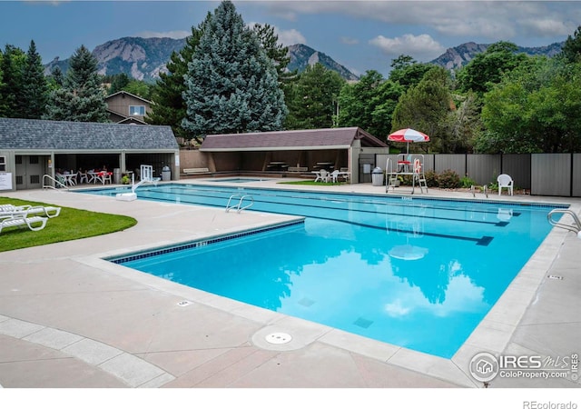 pool with fence, a mountain view, an outdoor structure, and a patio