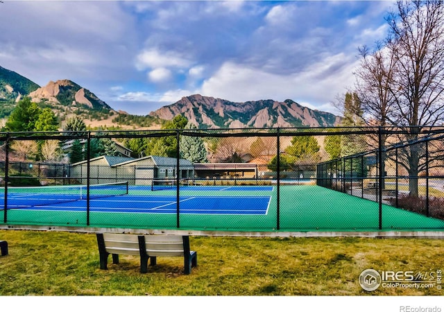 view of tennis court with fence, a mountain view, and a yard