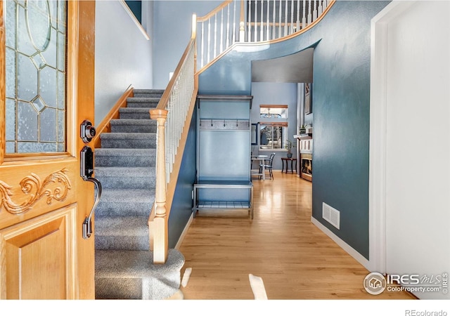 interior space featuring visible vents, stairway, a towering ceiling, wood finished floors, and baseboards