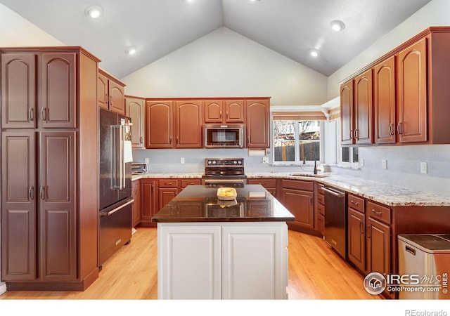 kitchen featuring dark stone counters, appliances with stainless steel finishes, a sink, and light wood-style flooring