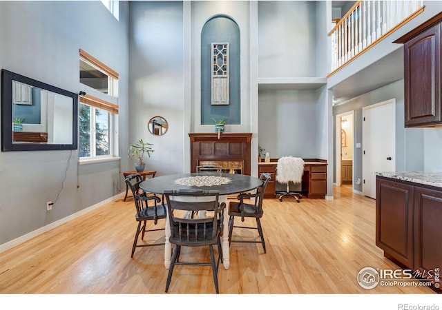 dining space with light wood-style flooring, a high ceiling, and baseboards