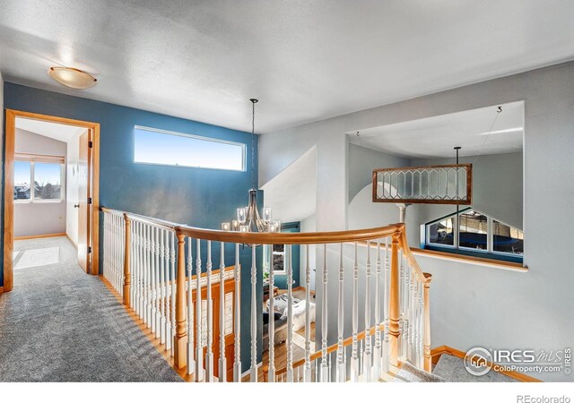 corridor with carpet, a chandelier, baseboards, and an upstairs landing