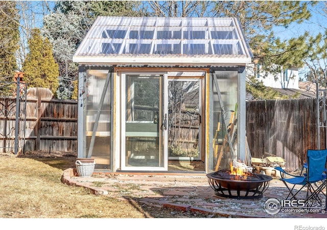 view of greenhouse with an outdoor fire pit and a fenced backyard