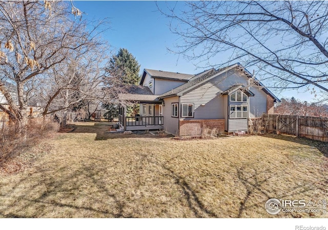 back of property featuring brick siding, a lawn, fence, and a wooden deck