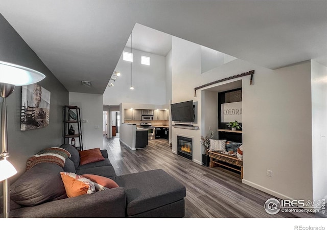 1004 Lucca Dr, Evans, CO 80620 - living room featuring a towering ceiling, a glass covered fireplace, visible vents, dark wood-style flooring, and baseboards