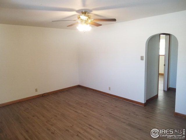 spare room featuring a ceiling fan, baseboards, arched walkways, and dark wood-type flooring